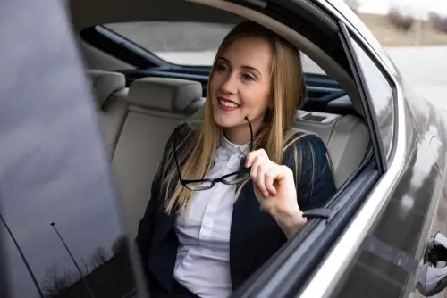 Young attractive business woman is holding her glasses while comfortably riding a black car service